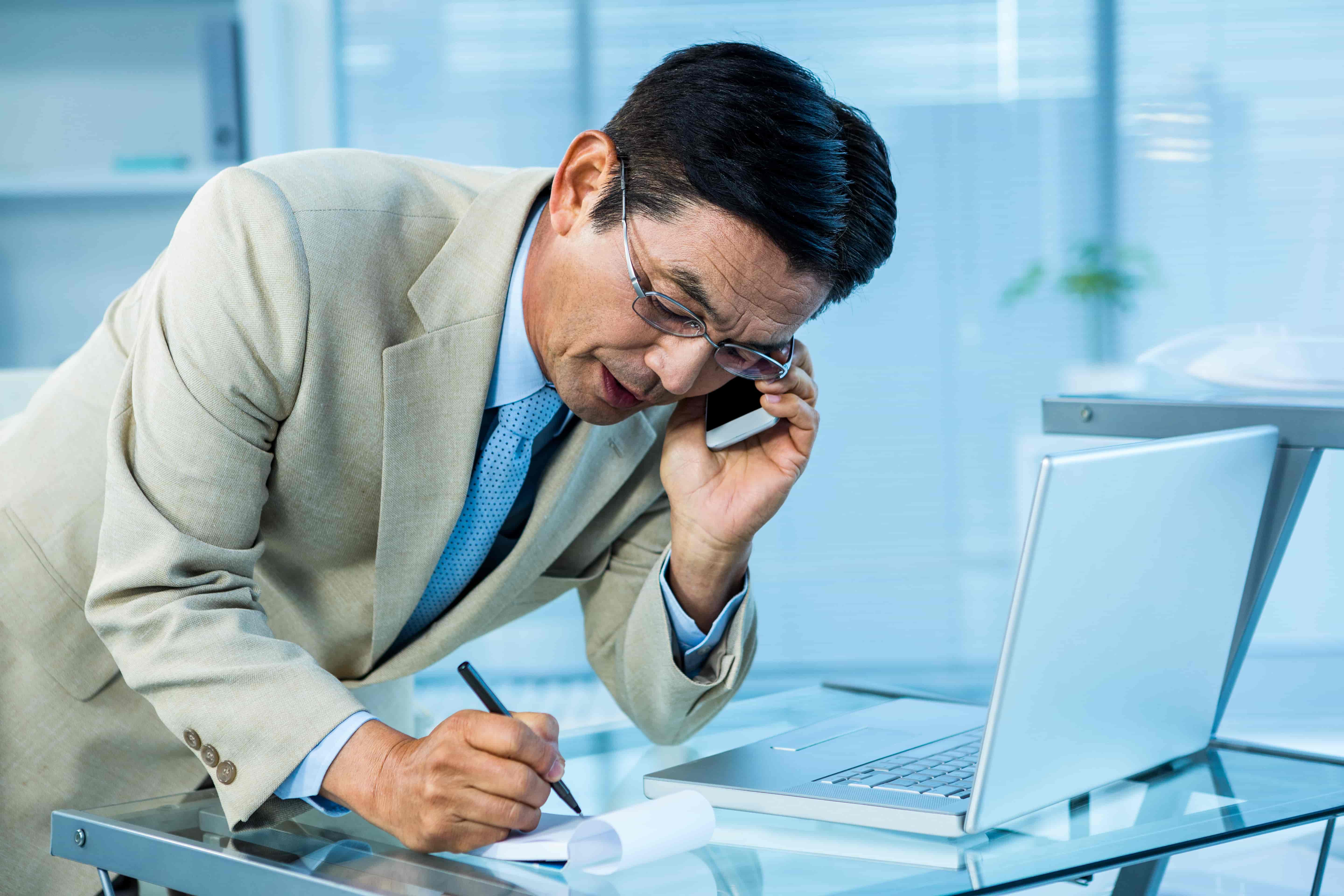 This is a photo of a man on his phone scribbling down notes.