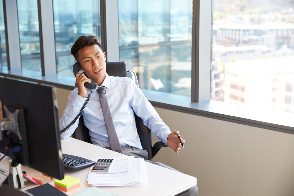 This is a photo of a Japanese business man making a phone call from his desk.